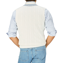 Person wearing an Off-White Blue Striped Cotton Cricket Slipover by Alan Paine over a blue and white striped shirt, paired with denim jeans, viewed from the back.