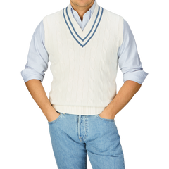 Man wearing a white Alan Paine Off-White Blue Striped Cotton Cricket Slipover over a blue-striped shirt with hands on hips.