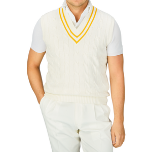 Man wearing an Alan Paine Off-White Yellow Striped Cotton Cricket Slipover with yellow and blue trim over a collared shirt, and white pants.
