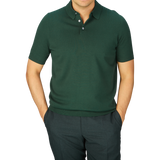 Man in a Alan Paine Racing Green Knitted Cotton Polo Shirt and dark trousers against a blue background.