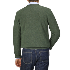 A person dressed in an Alan Paine Rosemary Green Lambswool V-Neck sweater and blue jeans is standing with their back to the camera.