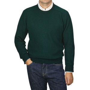 A man wearing an Alan Paine Tartan Green Lambswool Crew Neck sweater over a white collared shirt stands with his hand in his pocket against a plain light gray background.