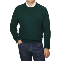 A man wearing an Alan Paine Tartan Green Lambswool Crew Neck sweater over a white collared shirt stands with his hand in his pocket against a plain light gray background.