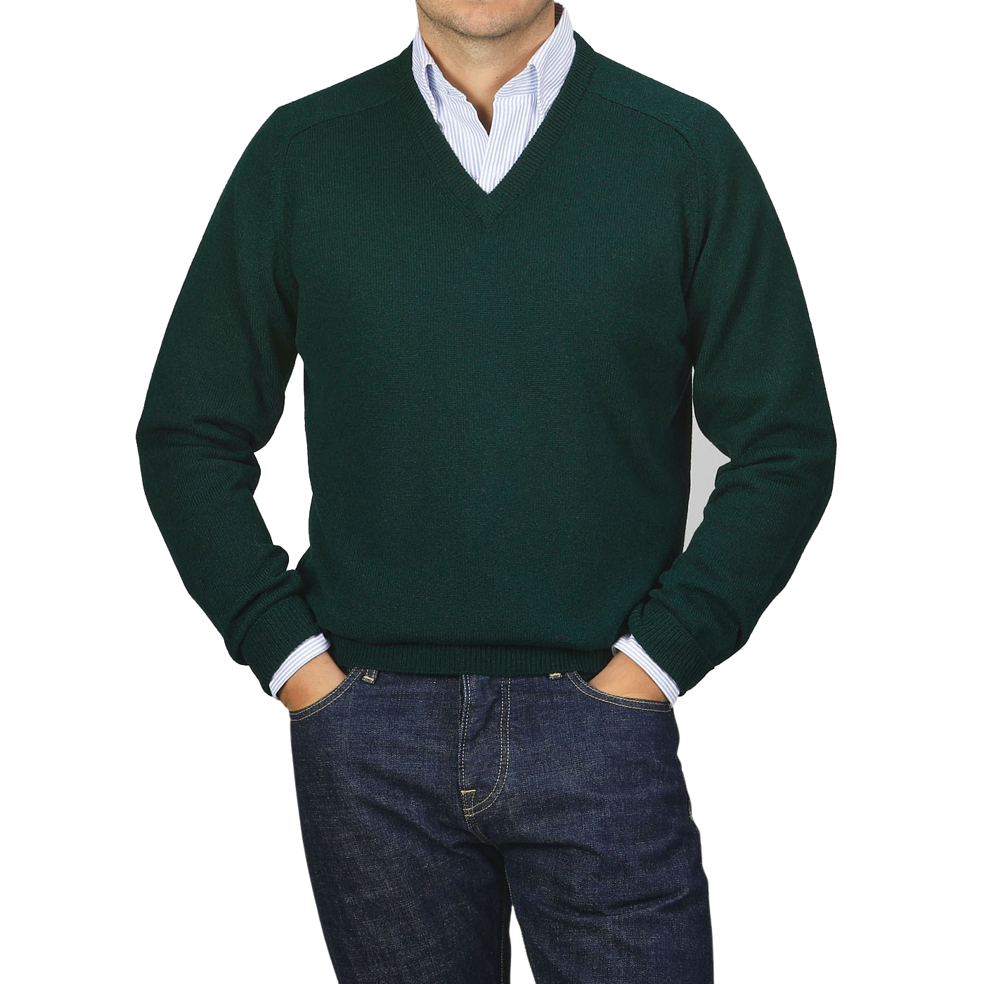 A person dressed in an Alan Paine Tartan Green Lambswool V-Neck sweater layered over a light blue collared shirt, paired with dark jeans, stands with their hands in their pockets against a plain gray background.