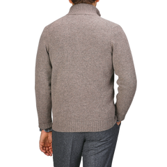 A person in a Taupe Beige Lambswool Landford Cardigan by Alan Paine and gray pants stands with their back against a gray backdrop.