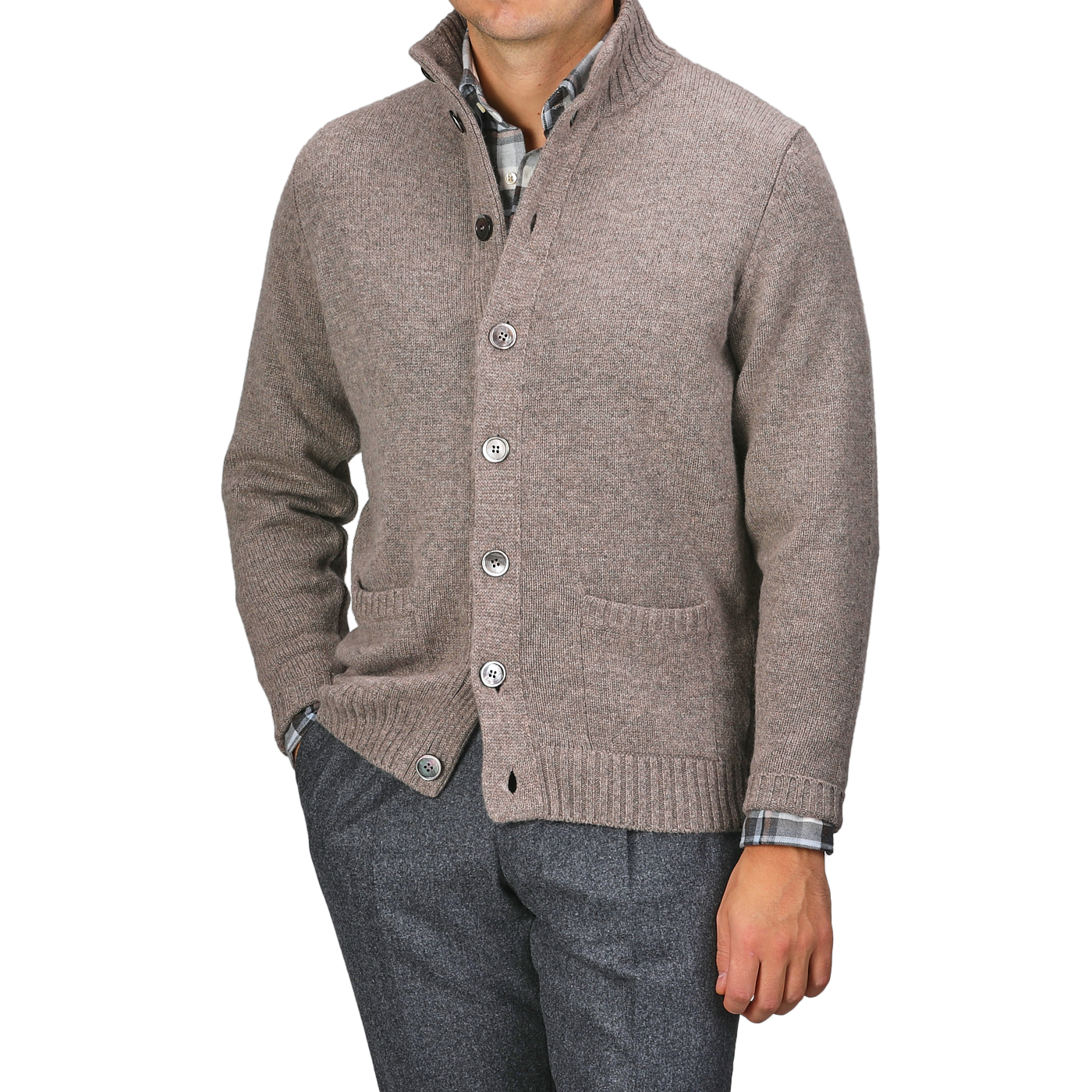 A person wearing an Alan Paine Taupe Beige Lambswool Landford Cardigan over a plaid shirt and gray trousers, with hands in pockets.