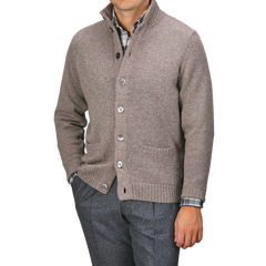 A person wearing an Alan Paine Taupe Beige Lambswool Landford Cardigan over a plaid shirt and gray trousers, with hands in pockets.