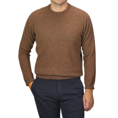 A person wearing an Alan Paine Tobacco Brown Lambswool Crew Neck and dark blue pants, with their left hand in their pocket.