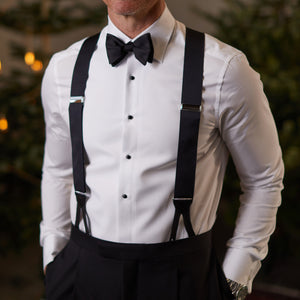 A man wearing Albert Thurston's Black Nylon Leather 40mm Braces and a bow tie in front of a Christmas tree.