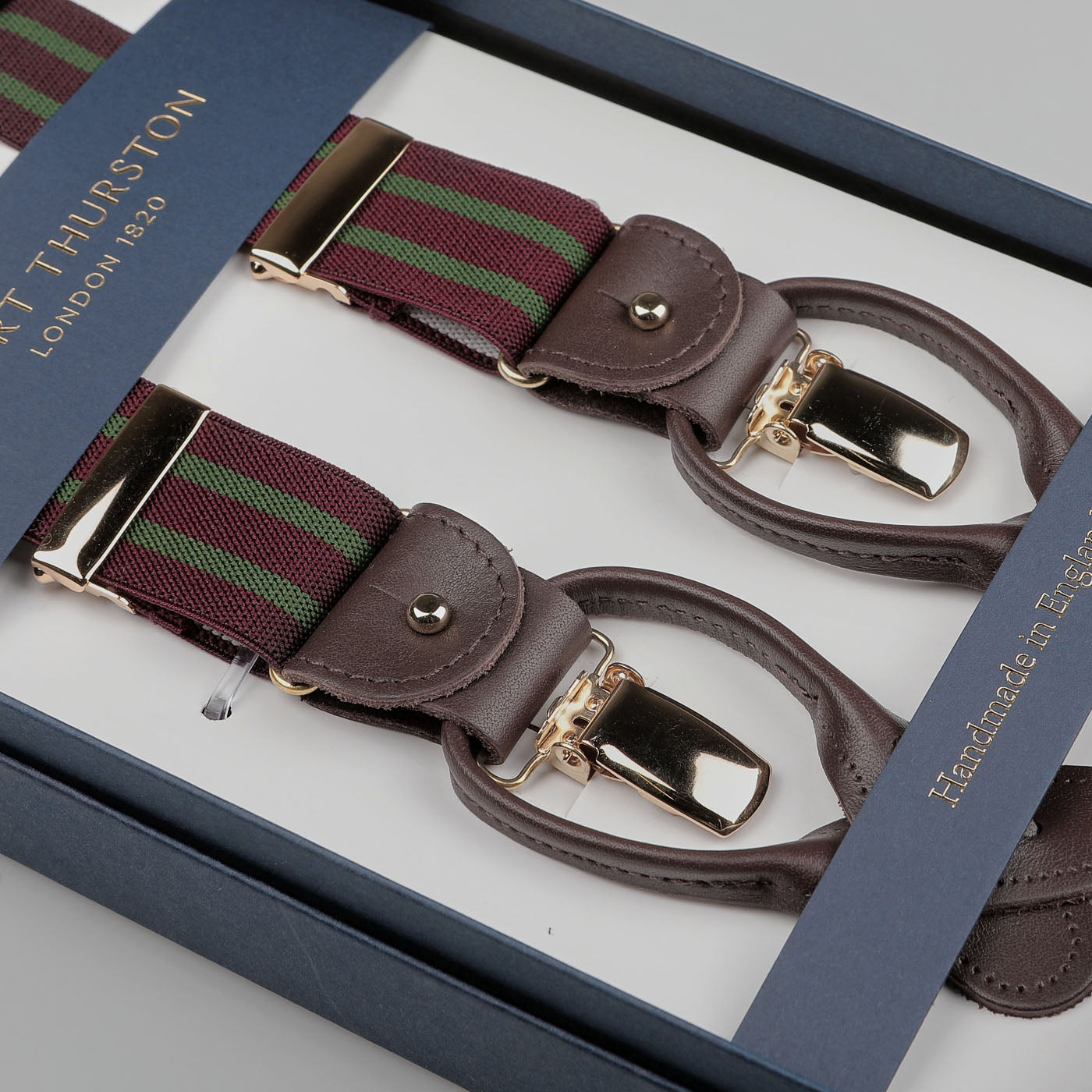 A boxed set of Burgundy Green Striped Nylon 30 mm Braces by Albert Thurston, featuring brown leather details and brass clasps, handcrafted in a stretchable nylon fabric.