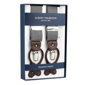 Box of "Light Grey Wool Fresco 35mm Braces" features gray fabric with brown leather details and metal clips. Labeled "Albert Thurston," it proudly states "Handmade in England," showcasing meticulous craftsmanship.