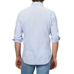 Sporting the Alessandro Gherardi Blue Wide Striped Cotton Single Cuff Shirt with rolled-up sleeves and a cut-away collar, a person pairs it with blue jeans and faces away.