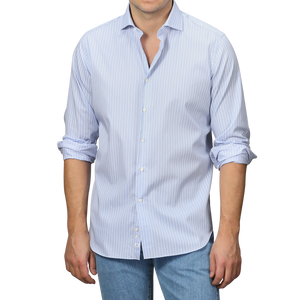 A man in an Alessandro Gherardi Blue Wide Striped Cotton Single Cuff Shirt with rolled-up sleeves is paired with jeans and stands against a gray background.