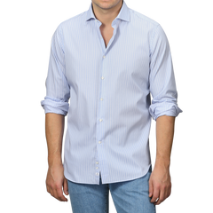 A man in an Alessandro Gherardi Blue Wide Striped Cotton Single Cuff Shirt with rolled-up sleeves is paired with jeans and stands against a gray background.