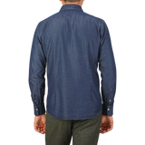 A person stands facing away from the camera, wearing an Alessandro Gherardi Dark Blue Cotton Denim Single Cuff Shirt and green trousers.