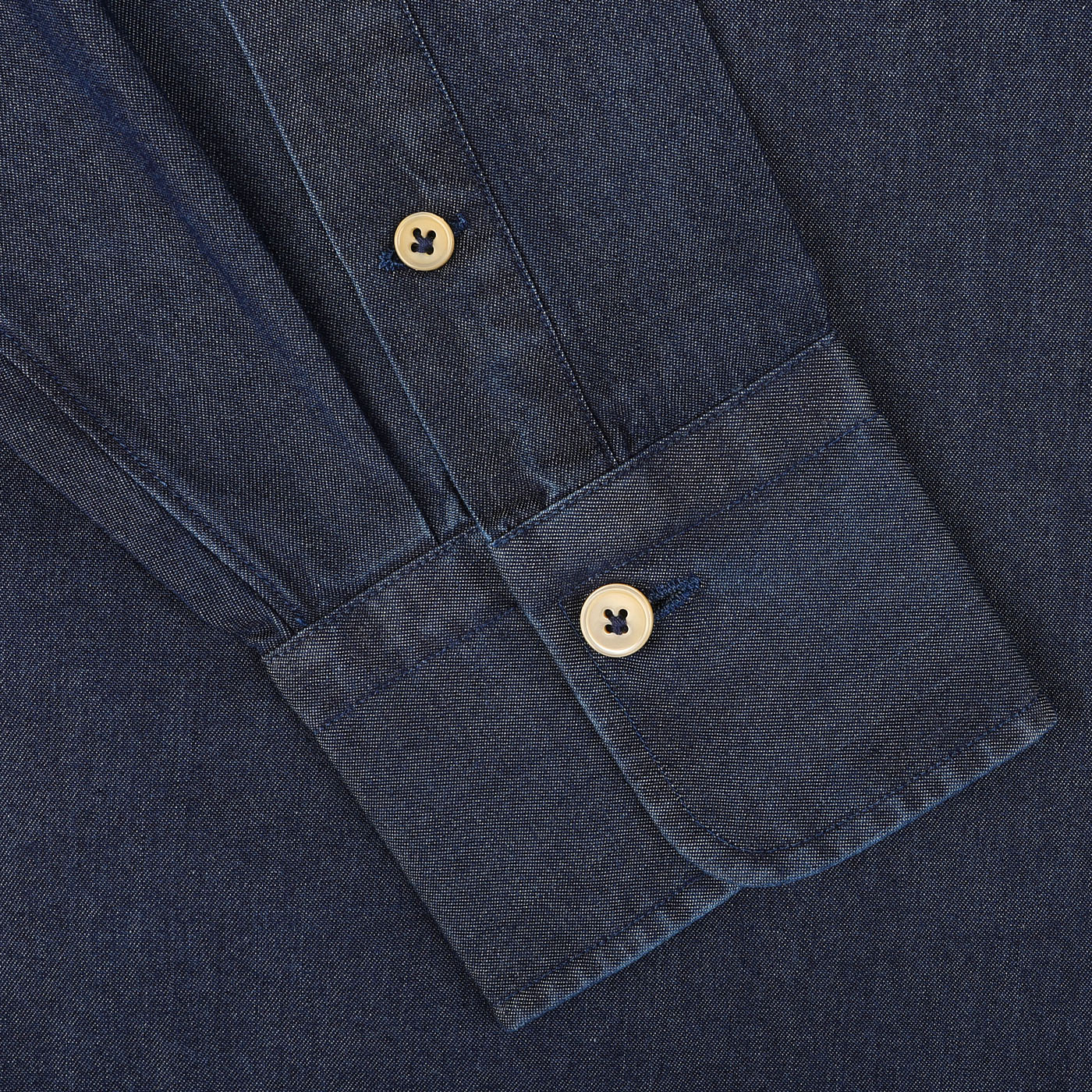 Close-up of an Alessandro Gherardi Dark Blue Cotton Denim Single Cuff Shirt sleeve, handcrafted from pure cotton and featuring two beige buttons on the cuff, lying flat against a matching dark blue denim fabric background.