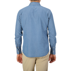 A person is standing with their back facing the camera, wearing an Alessandro Gherardi Light Blue Cotton Denim Single Cuff Shirt and beige pants.