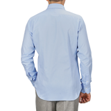 A person wearing an Alessandro Gherardi Light Blue Cotton Oxford Single Cuff Shirt and gray pants, facing away from the camera with one hand in their pocket.