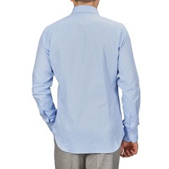 A person wearing an Alessandro Gherardi Light Blue Cotton Oxford Single Cuff Shirt and gray pants, facing away from the camera with one hand in their pocket.