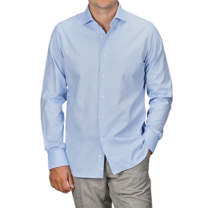 A person dressed in an Alessandro Gherardi Light Blue Cotton Oxford Single Cuff Shirt, with the sleeves down, and grey pants, standing with one hand in their pocket. The head is not visible.