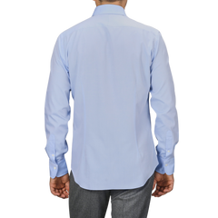 A person wearing a light blue Sky Blue Cotton Twill Single Cuff Shirt by Alessandro Gherardi and gray pants, viewed from the back.