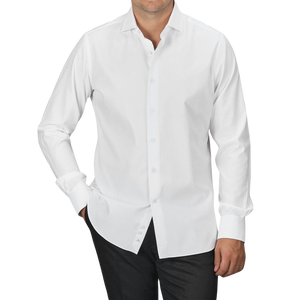 A man wearing an Alessandro Gherardi White Cotton Twill Single Cuff Shirt and black pants stands with his hands in his pockets against a plain gray background.