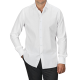 A man wearing an Alessandro Gherardi White Cotton Twill Single Cuff Shirt and black pants stands with his hands in his pockets against a plain gray background.