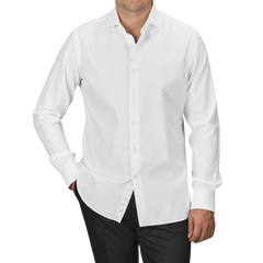 A man wearing an Alessandro Gherardi White Cotton Twill Single Cuff Shirt and black pants stands with his hands in his pockets against a plain gray background.