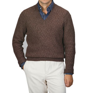 A person wearing an Altea Brown Wool Chevron Knit V-Neck over a blue denim shirt, paired with light beige pants.