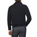 The image shows the back view of a person wearing a dark turtleneck sweater and blue jeans against a plain background, subtly hinting at the quality craftsmanship of an Altea Navy Blue Shetland Wool Button Cardigan.