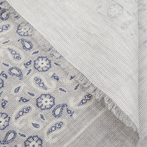 Close-up of a Amanda Christensen Grey Paisley Printed Linen Cotton Scarf peeking from beneath a folded white fabric.