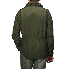 A person is seen from behind wearing Aspesi's Army Green Luxury Nylon Field Jacket featuring long sleeves and an adjustable waist, paired with grey pants against a plain background.