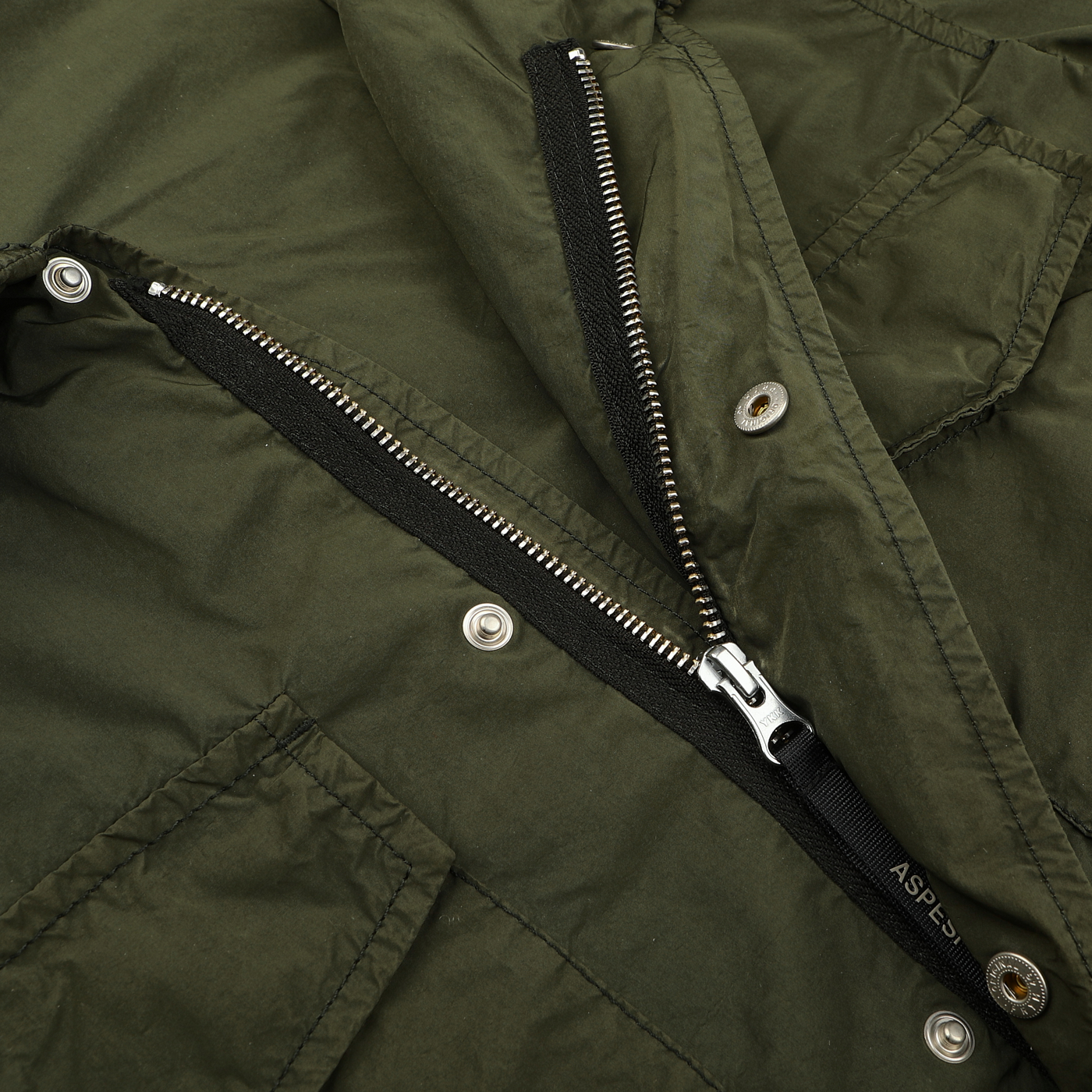 Close-up of an open zipper on an Army Green Luxury Nylon Field Jacket by Aspesi, showcasing its classic design often featuring silver buttons and a detachable hood for versatile wear.