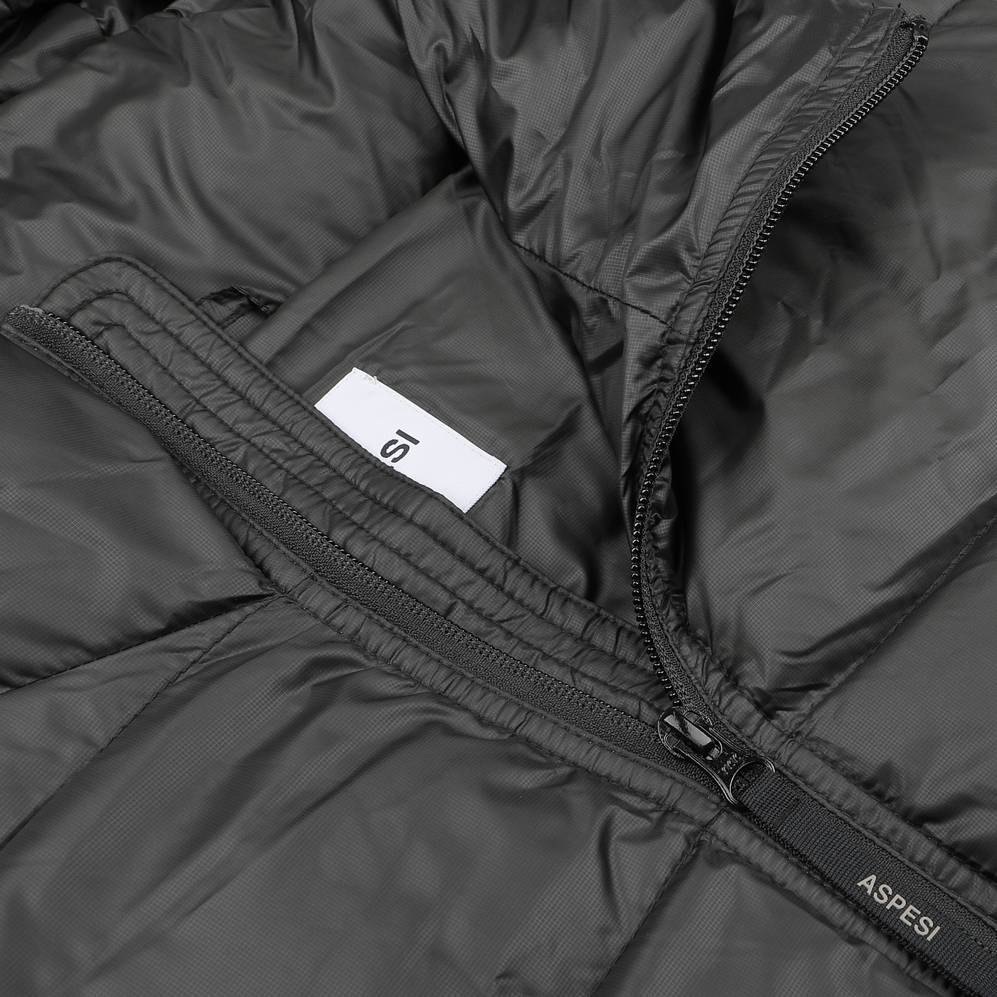 Close-up of a Black Nylon Ripstop Down Padded Budd Jacket by Aspesi, showcasing a partially open zipper that reveals a white tag inside. The jacket is constructed with durable nylon ripstop fabric for enhanced resilience.