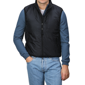 A man stands with his hands in his pockets, wearing the Aspesi Black Nylon Taffetta Thermore Jil Gilet over a blue long-sleeve shirt and blue jeans, set against a plain background.