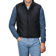 A man stands with his hands in his pockets, wearing the Aspesi Black Nylon Taffetta Thermore Jil Gilet over a blue long-sleeve shirt and blue jeans, set against a plain background.