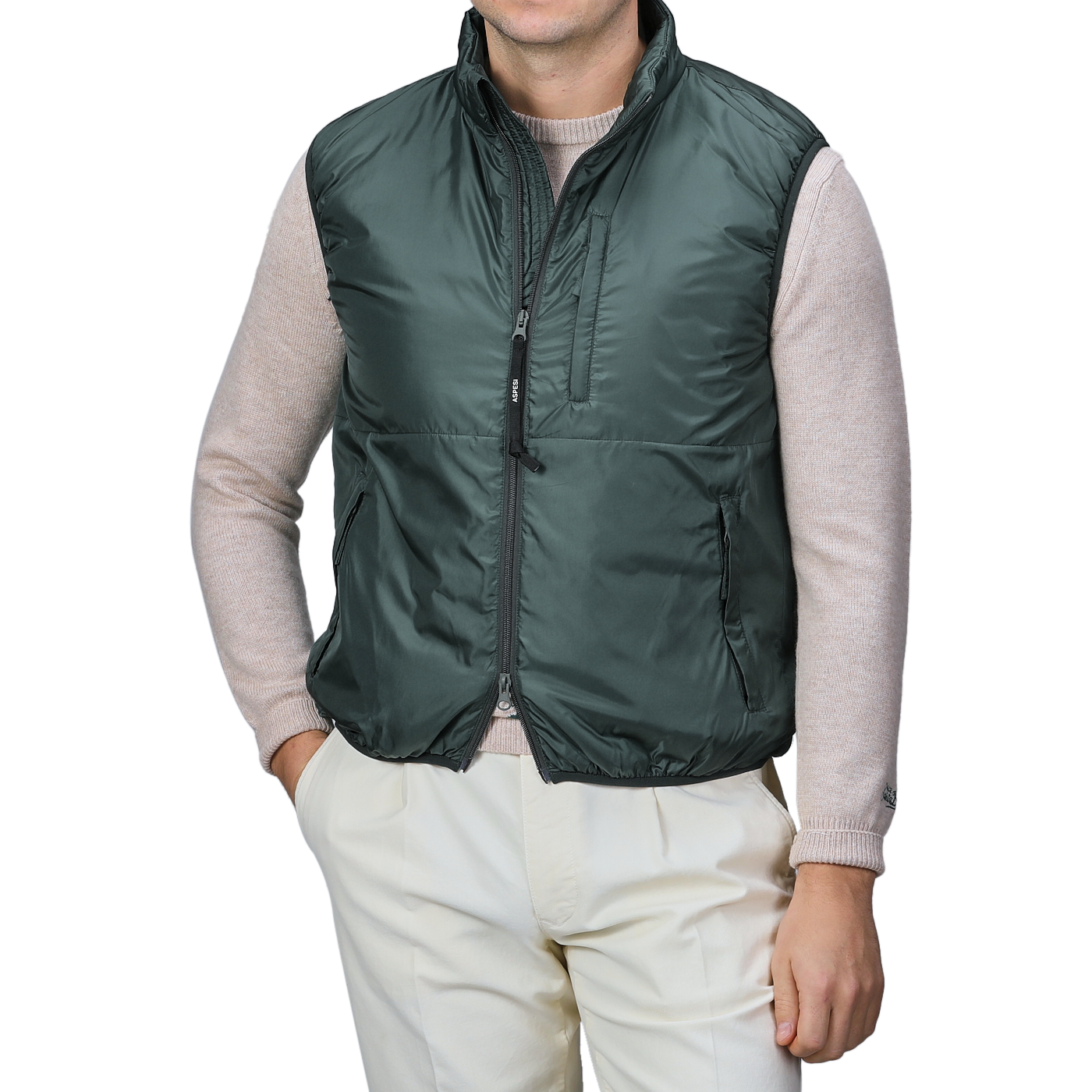 An individual sporting an Aspesi Bottle Green Nylon Taffeta Thermore Jil Gilet over a beige sweater and light trousers stands with one hand in their pocket.