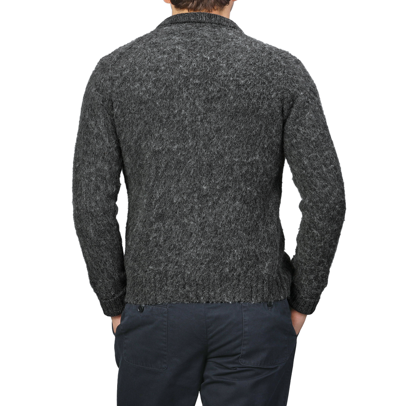 A man in a dark gray, textured sweater and dark pants stands with hands in pockets, facing away. The ensemble exudes classic elegance, reminiscent of the Aspesi Dark Grey Brushed Shetland Wool Cardigan's timeless appeal.