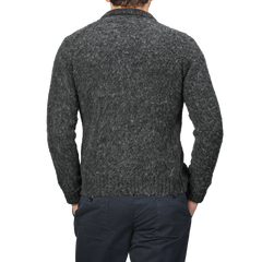 A man in a dark gray, textured sweater and dark pants stands with hands in pockets, facing away. The ensemble exudes classic elegance, reminiscent of the Aspesi Dark Grey Brushed Shetland Wool Cardigan's timeless appeal.