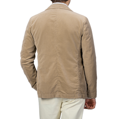 An individual is seen from behind, dressed in the Aspesi Light Beige Cotton Velvet Isaac Blazer paired with white pants, against a gray backdrop.