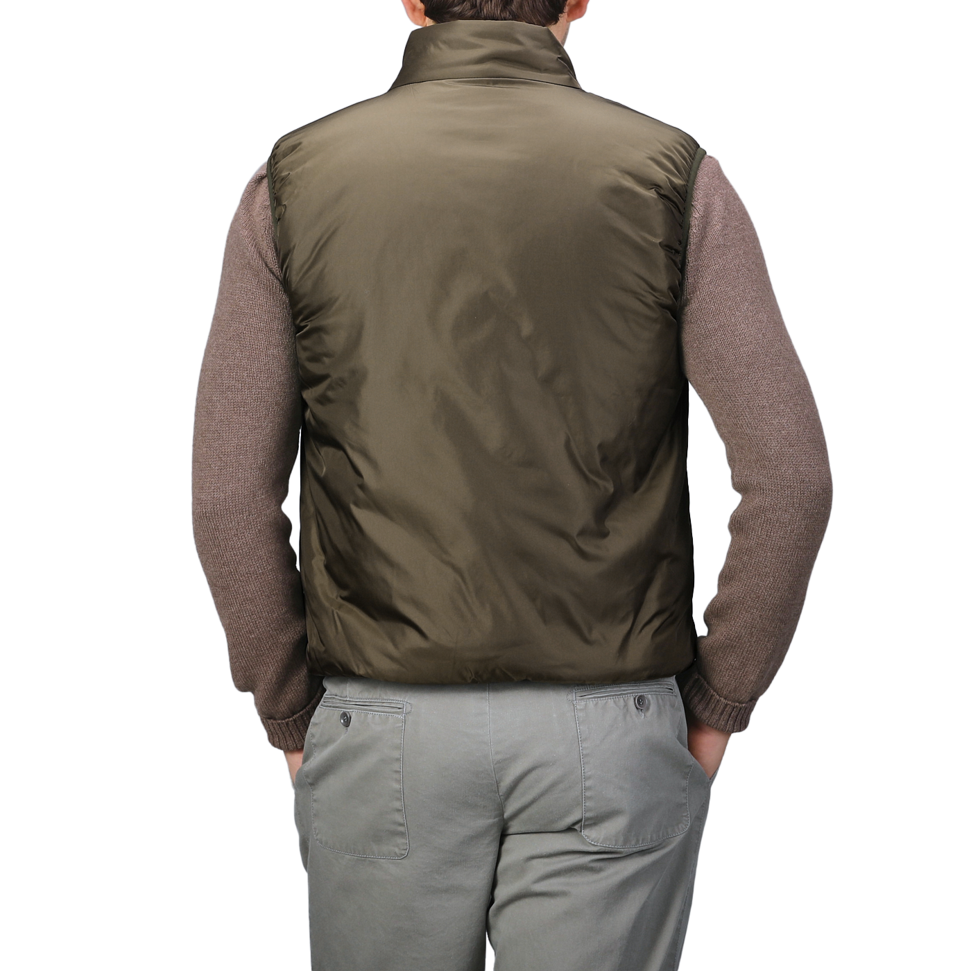 A person is seen from the back, wearing a brown sweater paired with light gray pants and an Aspesi Military Green Nylon Taffeta Thermore Jil Gilet, their hands in their pockets. The nylon taffeta exterior of the gilet suggests insulation with Thermore technical down for enhanced warmth and style.