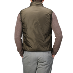 A person is seen from the back, wearing a brown sweater paired with light gray pants and an Aspesi Military Green Nylon Taffeta Thermore Jil Gilet, their hands in their pockets. The nylon taffeta exterior of the gilet suggests insulation with Thermore technical down for enhanced warmth and style.