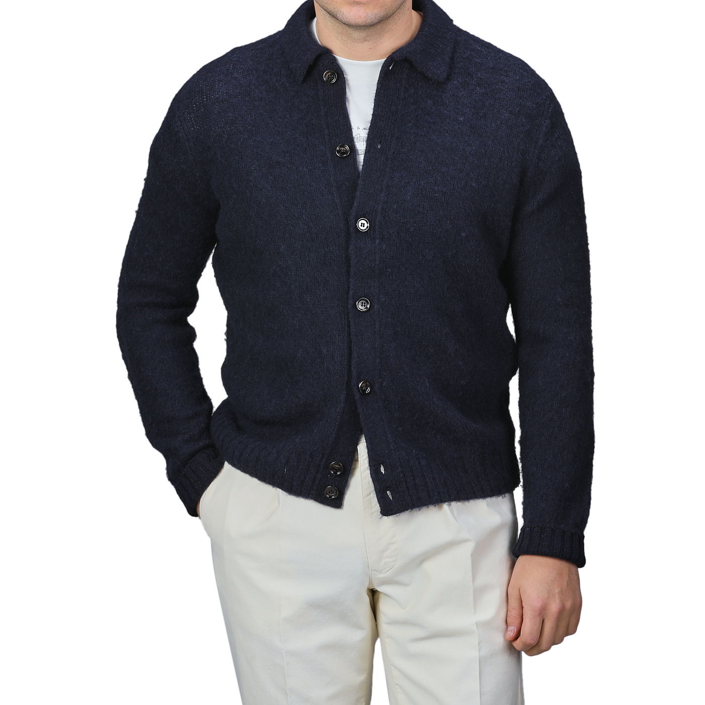 An individual dressed in an Aspesi Navy Blue Brushed Shetland Wool Cardigan, layered over a white shirt and complemented with beige pants, with the regular fit look finished off by casually tucking hands into pockets.