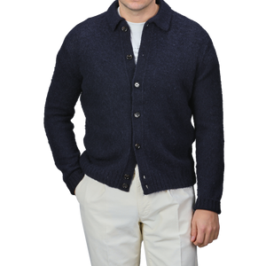 An individual dressed in an Aspesi Navy Blue Brushed Shetland Wool Cardigan, layered over a white shirt and complemented with beige pants, with the regular fit look finished off by casually tucking hands into pockets.