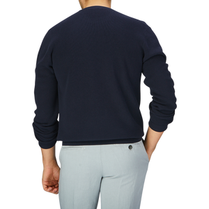 The back view of a man wearing a Aspesi navy blue knitted cotton sweater and grey pants.