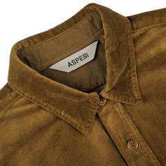 Close-up of the Tobacco Brown Cotton Velvet Overshirt by Aspesi, featuring a collar, buttons, and a label displaying the brand name "Aspesi." This casual alternative blazer crafted from pure cotton velvet exudes effortless style.