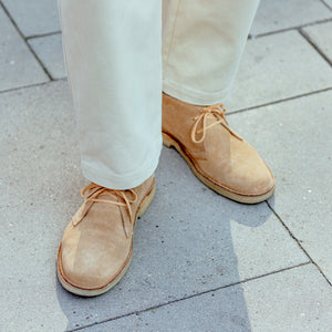 A person wearing a pair of Astorflex Cammello Beige Suede Driftflex Unlined Boots standing on a sidewalk.