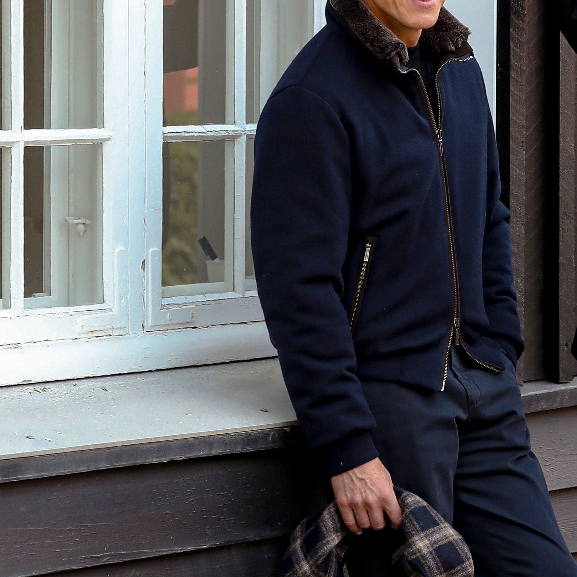 A person in a Moorer Navy Blue Cashmere Blend Down Padded Blouson is leaning against a windowsill, holding a plaid-patterned item.