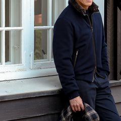 A person in a Moorer Navy Blue Cashmere Blend Down Padded Blouson is leaning against a windowsill, holding a plaid-patterned item.