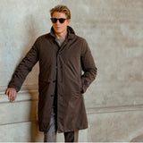 A person wearing sunglasses and a dark Marrone Brown Micro Nylon Thermore Coat by Aspesi stands against a concrete wall with one hand resting on the ledge.